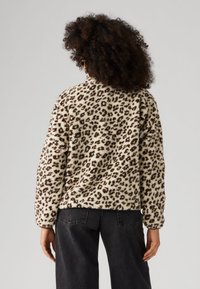 Ζακέτα από φλις με λεοπάρ μοτίβο σε μπεζ χρώμα με σκούρες καφέ κηλίδες. Χαλαρή εφαρμογή, μακρυά μανίκια, στρογγυλή λαιμόκοψη και απαλή υφή.