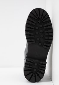 Černá gumová podrážka boty s hlubokým vzorkem, která má hexagonální vzory a boční šev. Velikost označená jako 37, s hladkým svrchním okrajem.