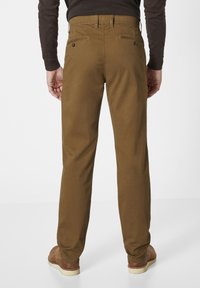 Braune Twill-Hosen mit geradem Schnitt, ausgestattet mit Gesäßtaschen und einer glatten Textur. Getragen mit braunem Schuhwerk, schlichter Hintergrund.