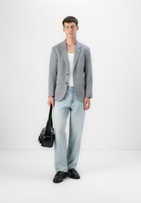 Gray tailored blazer over a white tank top, paired with light blue wide-leg jeans and black leather shoes. Holds a black leather bag.