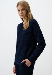 Marineblaue Langarmbluse aus strukturiertem Stoff mit einem Waffelstrickmuster, rundem Ausschnitt und lockerem Schnitt mit seitlichen Taschen.