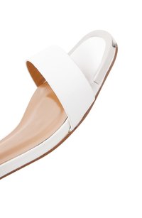 Chancla blanca con una tira ancha, punta descubierta y acento metálico. La suela es de color marrón claro, con una textura suave y forma curva.