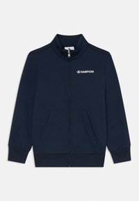 Tamno plava jakna na zip od mekog materijala s visokim ovratnikom, središnjim zatvaračem i dva prednja džepa. Ima "Champion" logo na prsima.