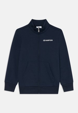 Veste zippée bleu marine en tissu doux avec col haut, fermeture éclair au centre et deux poches avant. Présente le logo "Champion" sur la poitrine.
