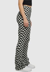 Schwarz-weiß karierte, ausgestellte Hose aus dehnbarem Stoff, mit hoher Taille und glatter Textur. Getragen mit weißen Sneakers.
