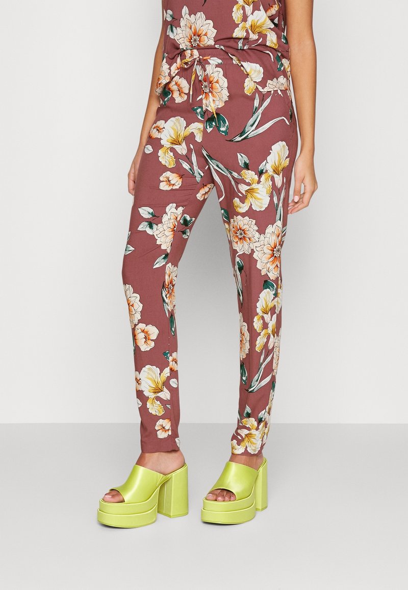 Pantalon bordeaux à imprimé floral avec des fleurs vertes, jaunes et blanches, associé à des sandales à plateforme vert lime à bouts ouverts et talons hauts.