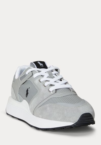 Baskets de sport grises et blanches avec lacets blancs, empiècements en mesh et en daim, logo noir sur le côté, et semelle blanche amortie avec semelle extérieure noire.