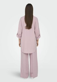 Ensemble en lin violet clair comprenant une longue chemise ample avec des épaules tombantes et un pantalon large, mettant en avant une texture lisse et un design minimal.