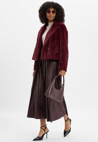 Burgunderfarget faux fur kort jakke, ribbestrikket kremfarget topp, mørkebrun plissert skinnskjørt, svarte spisse hæler, og en lavendel håndveske.