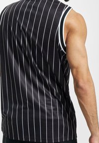 Maglietta nera senza maniche con righe verticali bianche, caratterizzata da una texture liscia e una bordatura bianca a contrasto attorno alle aperture delle braccia.