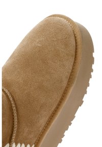 Lichtbruine suède schoen met een ronde neus, beige rubberen zool en contrasterende witte stiksels langs de naad.