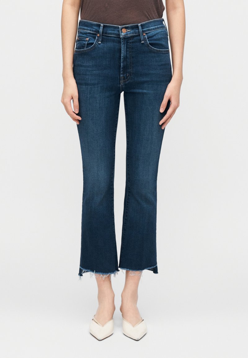 Tumed sinised kõrge vöökohaga laiade säärtega teksapüksid, millel on töödeldud ääred, sile tekstuur ja õrnad triibud reitel. Kandmisega koos beežide kontsakingadega.