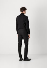 Melnas garās piedurknes turtlenecks krekls, kas apvienots ar pieguļošām melnām biksēm un melnām apaviem, demonstrējot elegantu, plūstošu siluetu.