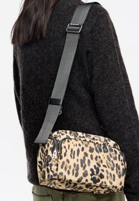 Bolso bandolera con estampado de leopardo, que cuenta con dos compartimentos con cremallera, elaborado en tejido texturizado, y presenta una correa ajustable gris con acentos en negro.