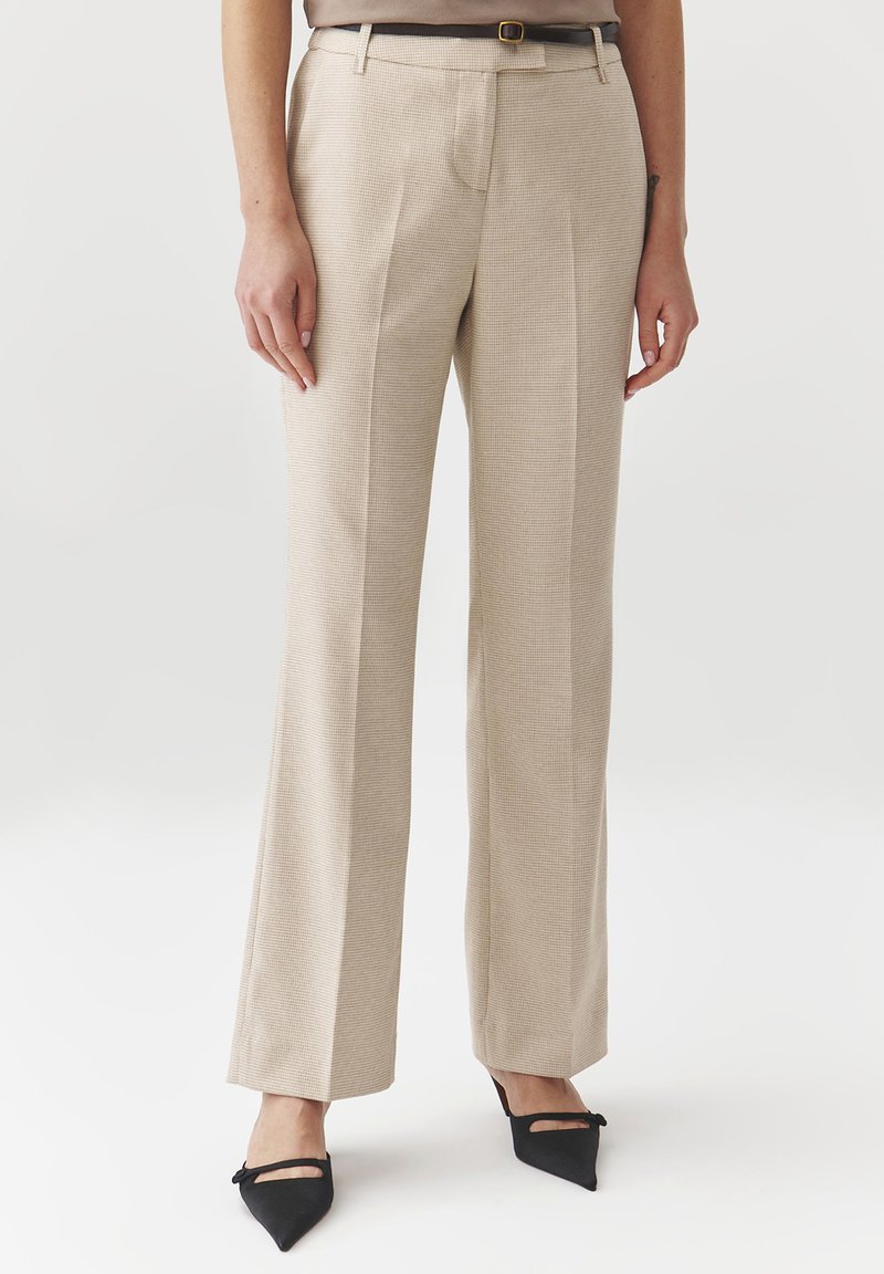 Pantaloni beige su misura in tessuto testurizzato, con un design a gamba dritta e pieghe frontali. Abbinati a tacchi a punta nera.