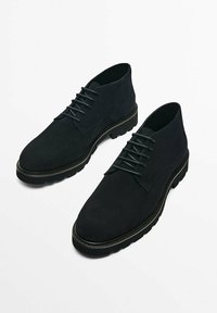 Svarta mockaskor med låg skärning, snörning och strukturerade gummisulor. Har en rundad tå och en minimalistisk stil.