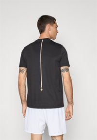 Svart trenings T-skjorte med gull vertikal glidelås på ryggen, kort erme, og rund hals, kombinert med hvite shorts.