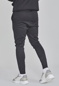 Pantaloni sportivi neri con un design aderente, realizzati in materiale elasticizzato. Abbinati a scarpe da ginnastica bianche con accenti grigi e dettagli testurizzati.