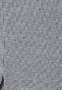 Grauer Stoff mit feiner Strickstruktur und einem dezenten Muster. Das Material wirkt weich und leicht dehnbar, mit sauberen Nähten.