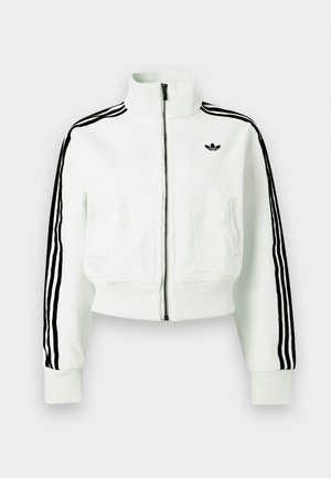 Λευκό κοντό μπουφάν με ψηλό γιακά, μπροστινό φερμουάρ, μαύρες ρίγες στα μανίκι α και μικρό μαύρο λογότυπο στο στήθος.