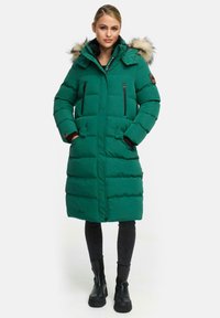 Zelena puffer jakna s kapuco obloženo s krznom, žepki z zadrgo, srednja dolžina in vertikalna strukturirana oblika. Nosite jo preko črnih hlač in čevljev.