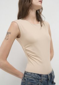 Body aderente color carne con scollatura rotonda, maniche a cappuccio e arricciature sulla cucitura laterale, abbinato a shorts in denim a vita alta.