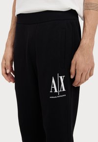 Schwarze Jogginghose aus weichem Stoff mit subtiler Textur. Enthält das weiße "AX"-Logo und den Text "ARMANI EXCHANGE" am Oberschenkel sowie Seitentaschen.