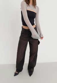 Top corto nero con maniche lunghe trasparenti e scintillanti; abbinato a jeans larghi in denim scuro e scarpe con tacco a punta nere.