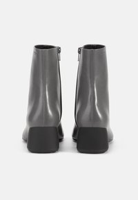 Botas de tobillo de cuero gris con un acabado brillante, tacón cuadrado negro y cierre de cremallera en la parte trasera. Diseño minimalista con líneas limpias.