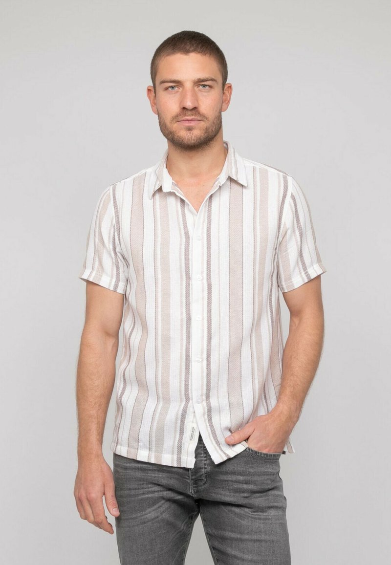 Chemise à manches courtes avec boutonnière, en blanc et rayures verticales marron clair, en tissu texturé, avec un col en V et un ourlet droit.