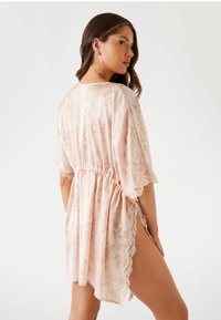 Lichtroze kimono-stijl cover-up gemaakt van doorschijnende stof. Kenmerkt zich door een bloemendessin, elastische taille en kantafwerking op de mouwen en zoom.