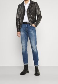 Černá kožená motorkářská bunda, bílá polo košile, modré džíny s ohrnutými manžetami a černé kotníkové boty. Jednoduch�ý, slim fit design a hladké textury.