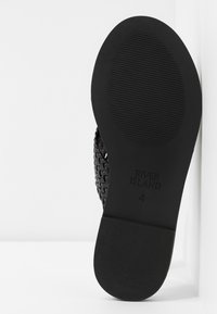 Sandale tissée noire avec une semelle en caoutchouc plate à texture côtelée. Nom de la marque "RIVER ISLAND" et taille "4" embossés sur le dessous.