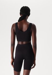 Zwarte sportbeha met een textuurdesign en een ronde halslijn, gecombineerd met hoge zwarte fietsshorts, beide strak en naadloos.