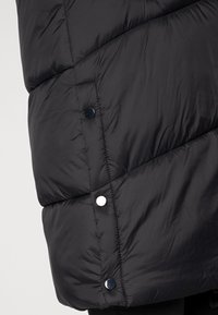 Svart pufferjacka med en diagonal quiltad design, mjuk textur och silverfärgade tryckknappar för stängning, som framhäver värme och funktionalitet.