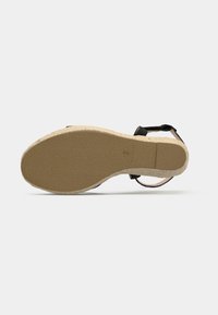 Black sandal with a textured rubber sole, featuring ankle straps and a woven jute midsole, showcasing an open design and adjustable buckle.