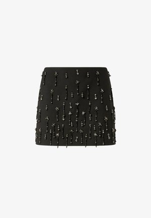 Gonna nera con silhouette aderente, arricchita da decorazioni con perline a motivi floreali e lunghezze variabili sulla superficie.