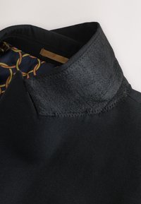 Black garment with a wool collar and smooth fabric. Inner lining features a navy background with circular patterns in orange and yellow.