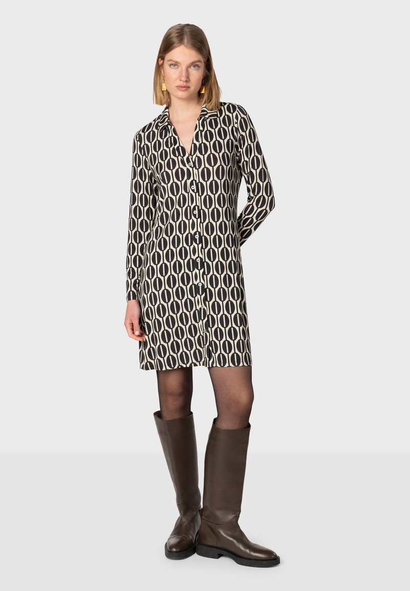 Vestito a camicia con un motivo ovale nero e crema, maniche lunghe e taglio dritto, abbinato a stivali alti in pelle marrone.