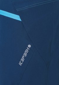 Pantalones deportivos de color azul marino con una textura suave, que presentan una cremallera en un tono azul claro y un logotipo reflectante en el lado.