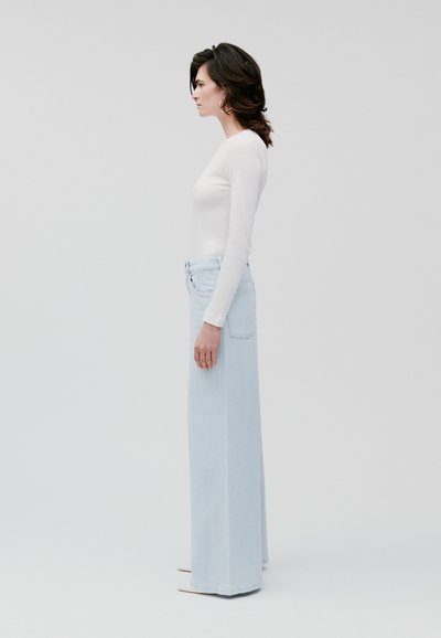Pantaloni in denim blu chiaro a gamba larga, a vita alta, con un classico design a cinque tasche e un taglio dritto, abbinati a una maglietta bianca a maniche lunghe.