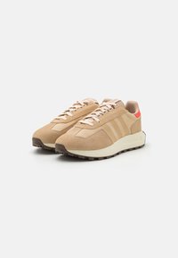 Beige mockalädersneakers med en texturerad ovandel, rosa inslag, snörning och en vit mellansula. Sulan har ett mönstrat greppmönster för bättre fäste.