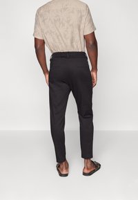 Czarne, dopasowane spodnie o wąskim kroju z elastycznym pasem. Teksturowany, lekki materiał posiada dwie tylne kieszenie. Noszone z beżową, wzorzystą koszulą.