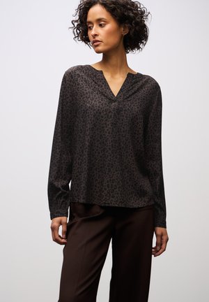 Dunkel Leopardenmuster-Bluse mit V-Ausschnitt und langen Ärmeln, aus glattem Stoff gefertigt. Getragen mit braunen Hosen, die einen lockeren Schnitt haben.