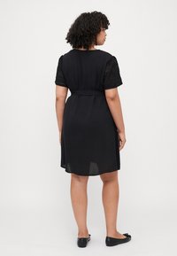 Black dress with short textured sleeves, a belted waist, and a knee-length cut. Worn with simple black flats. Smooth fabric, casual design.