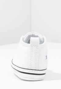 Białe płócienne buty z teksturowaną powierzchnią, z czarną paskiem wokół podeszwy i okrągłym logo po zewnętrznej stronie.