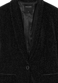 Blazer in velluto nero con motivo testurizzato, chiusura a un bottone e due tasche frontali. Fodera interna liscia e nera. Etichetta del marchio visibile.