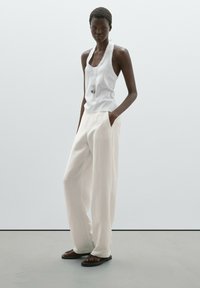White sleeveless tank top and loose-fitting, cream wide-leg trousers. Accessories include a pendant necklace and black sandals. Smooth fabric texture.
