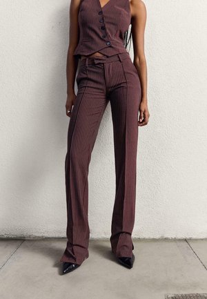 Bordeaux gestreepte mouwloze top met v-hals en knopen, gecombineerd met bijpassende flared broek. Kenmerkt puntige zwarte hakken. Glad textuur.