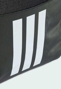 Mustapohjainen urheilukassi, jossa on kolme näkyvää valkoista raitaa, valmistettu kestävästä materiaalista, jossa on sileä pinta. Yksinkertainen ja moderni muotoilu.